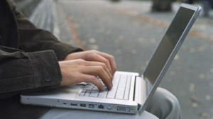 Young man using laptop on park bench, autumn, side view, mid section